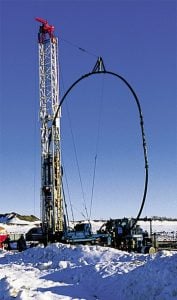 Heavy drilling rig working in snowy outdoor environment with pipe for oil or gas extraction.